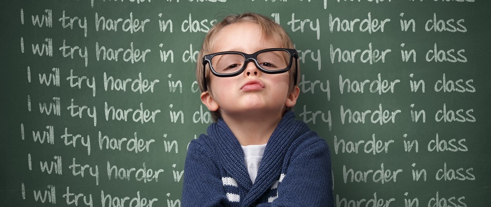 Young boy at school in front of "I will try harder" on chalk board