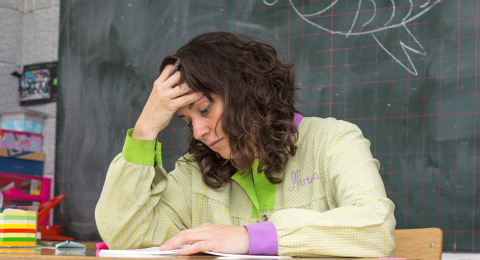 Tired looking teacher reading paperwork in a classroom 