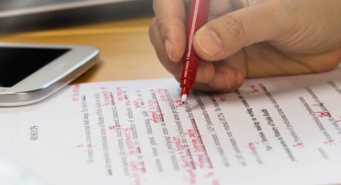 person holding red pen and marking a paper