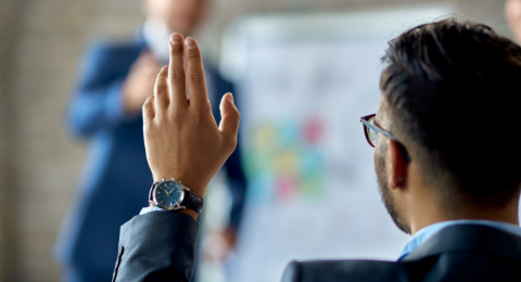 man in suit raising hand at a meeting