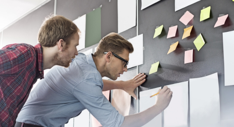 men working at board filled with papers and sticky notes