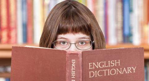 girl with glasses peering over the top of a dictionary