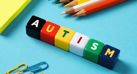 The word autism spelled out in colorful blocks near paperclips and pencils