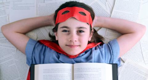 Child in a superhero costume reclining on book pages