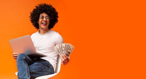 happy seated person holding money and laptop