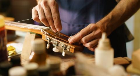a person's torso and two hands doing work on the neck of an acoustic guitar