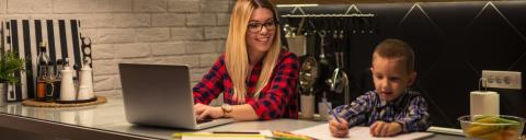 A young mother and child in plaid shirts both working on top of a kitchen table