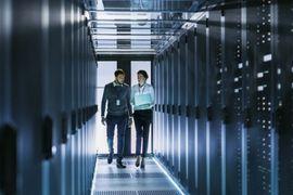 Two people walking between rows of data storage