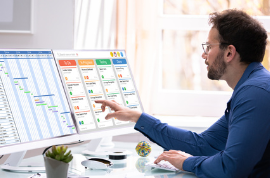 Person pointing at graphs and charts on one of two monitors