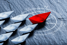 red paper ship leading other blue ships